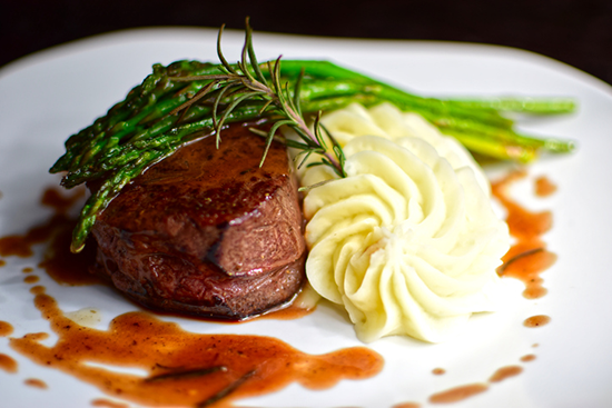 A perfectly plated filet mignon steak with sauce, whipped potatoes, and tender pencil asparagus.